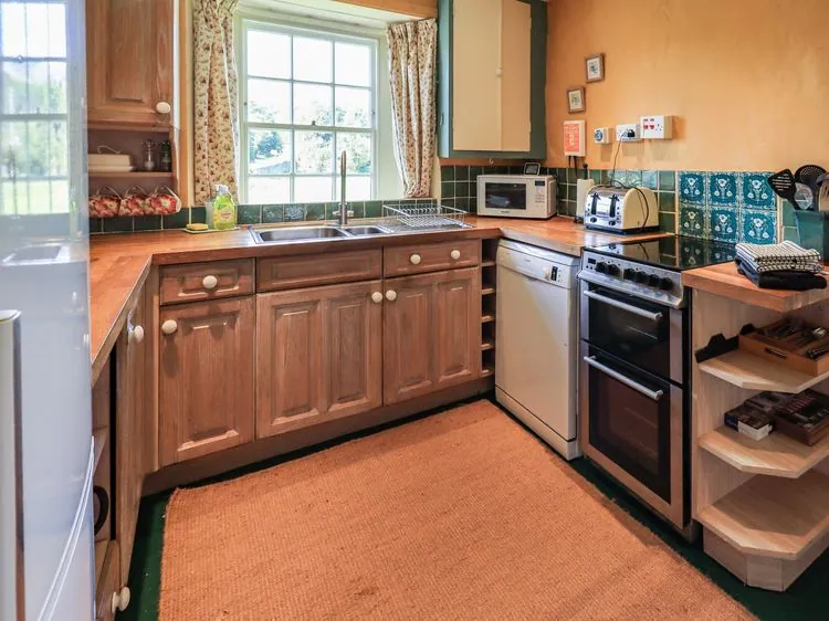 A kitchen with wooden cabinets a sink dishwasher oven microwave and toaster at Ellis Howe in Torver